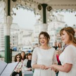 brides smiling during their vows under a bandstand with guests in the background