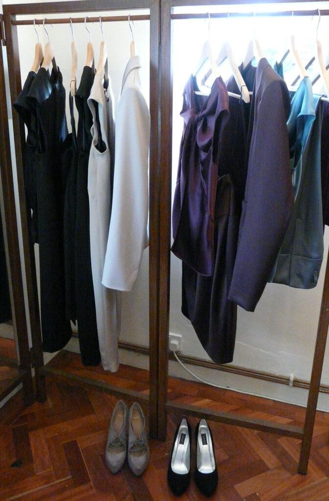 Image shows a number of smart tailored garments hanging on a clothes rail with pairs of high heels