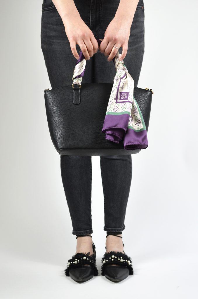 Model holding a bag with Silk scarf in Suffragette colours printed with inspiring quotes by women in history tied around the handle