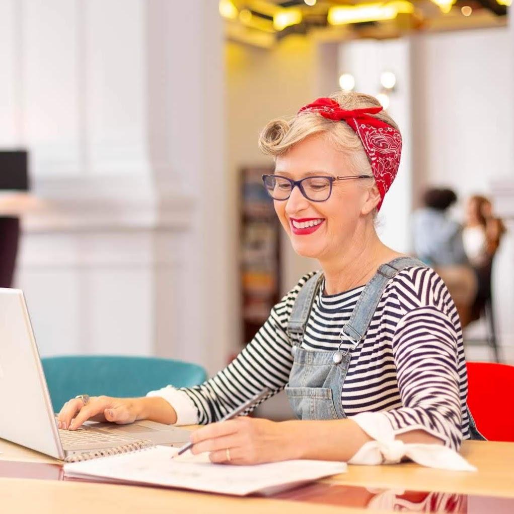 Stylist Ghislaine Walker sitting at her desk wearing a striped t shirt denim dungarees and a red bandana tied around her head