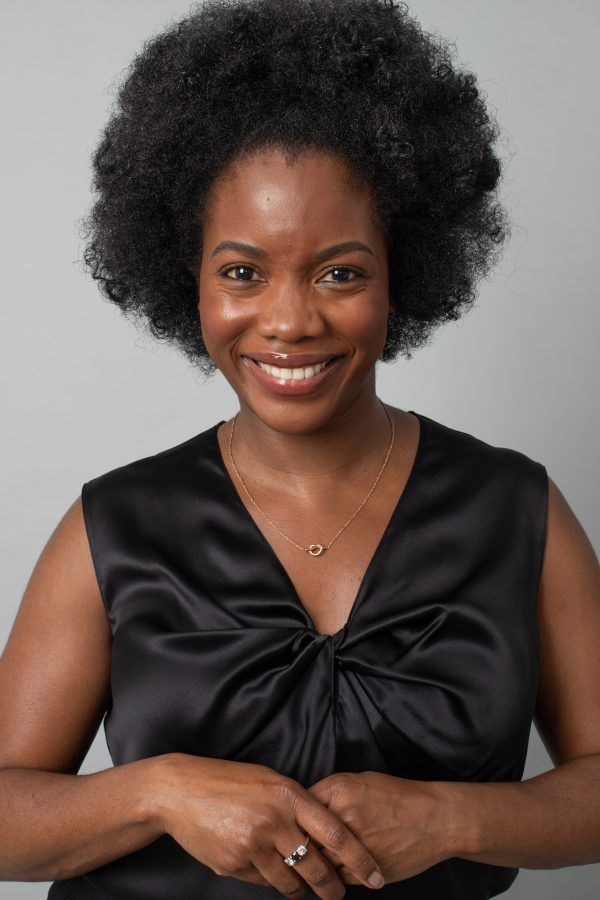 Close up of black woman smiling into the camera modelling black silk camisole blouse. Blouse is twisted and draped at bust level.