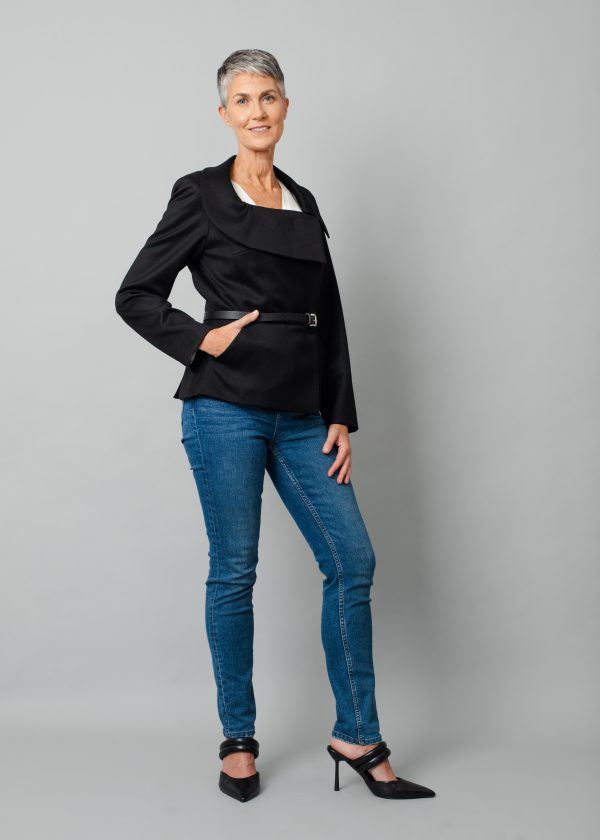 Grey short haired model wearing black jacket styled with a belt, blue jeans and black high heels