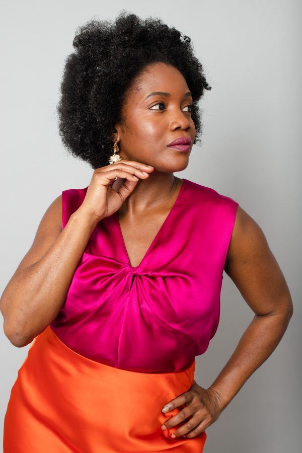 Black woman with afro hairstyle modelling pink silk camisole and orange satin skirt.