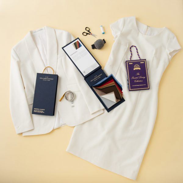 Flat lay of ivory tailored dress and blazer with cloth swatches tape measure pin cushion and dressmaking scissors