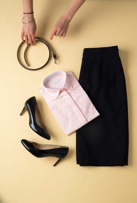 Flat lay of tailored black pencil skirt pink tailored shirt and black high heels with belt