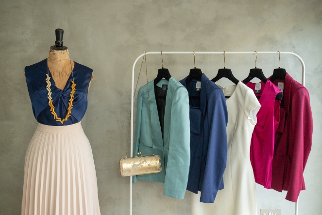 Close up image of Dara Ford tailored outfits with a skirt and camisole on a dressmakers dummy jackets a camisole and a dress hanging on a rail and a clutch bag