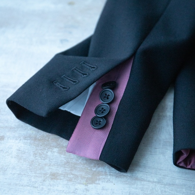 Close up of a black tailored jacket cuff with buttons and purple seam with cream lining