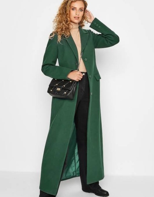 White Tall model wearing green full length wool coat black trousers and camel turtleneck with a black padded cross body bag