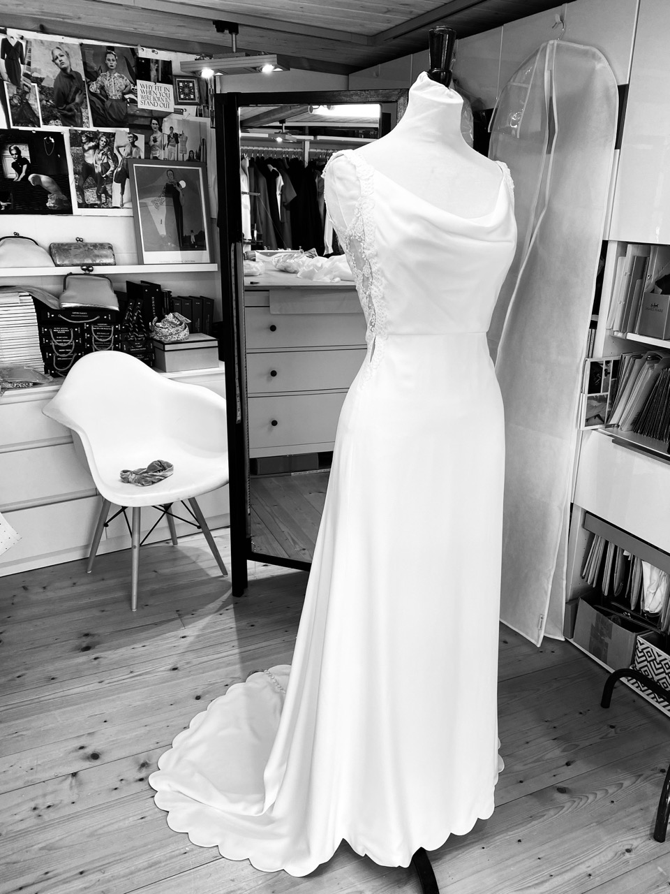 Black & white image of a bespoke silk wedding dress with lace side panels, cowl neck, mid-length train and scalloped hem on a mannequin in the Dara Ford tailoring studio