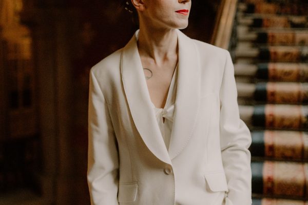 A white bridal model with bright red lips in an ivory trouser suit, and silk camisole